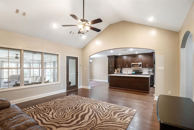 living area with visible vents, arched walkways, ceiling fan, dark wood-type flooring, and high vaulted ceiling