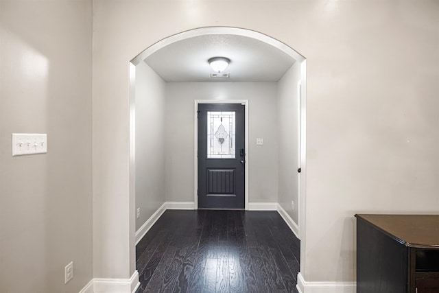 foyer entrance featuring dark wood-style floors, arched walkways, visible vents, and baseboards