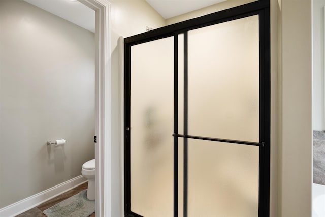 full bathroom featuring a stall shower, wood finished floors, toilet, and baseboards