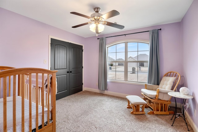 carpeted bedroom with a crib, ceiling fan, baseboards, and a closet