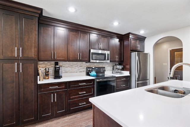 kitchen featuring arched walkways, appliances with stainless steel finishes, a sink, light countertops, and backsplash