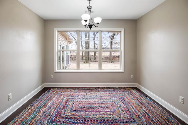 unfurnished dining area featuring dark wood-style floors, baseboards, and a notable chandelier