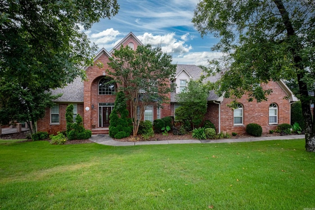 traditional home with brick siding, a front lawn, and roof with shingles