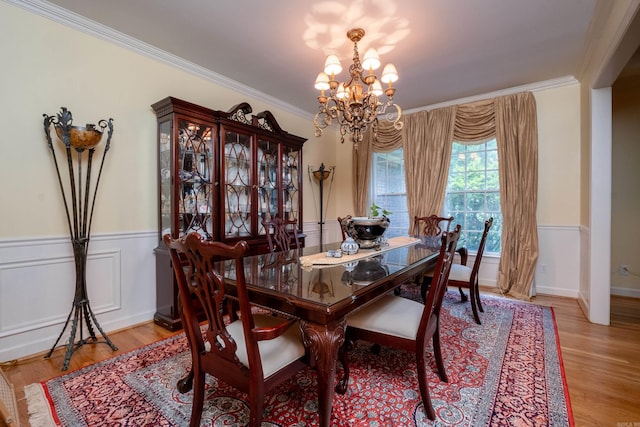 dining space with a wainscoted wall, a chandelier, light wood finished floors, and ornamental molding