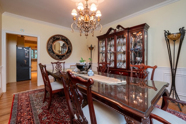 dining room with ornamental molding, wainscoting, an inviting chandelier, and wood finished floors