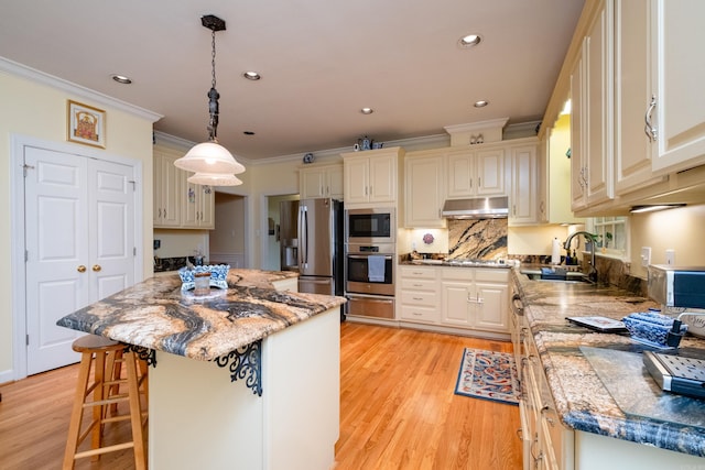 kitchen featuring stainless steel appliances, light wood-style flooring, ornamental molding, a sink, and under cabinet range hood