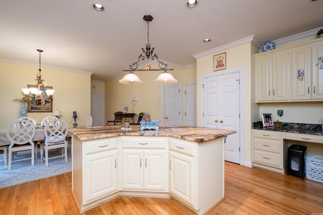 kitchen with light stone counters, a center island, built in desk, hanging light fixtures, and light wood-style floors