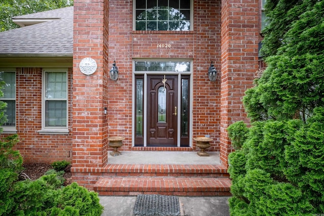 view of exterior entry featuring a shingled roof and brick siding