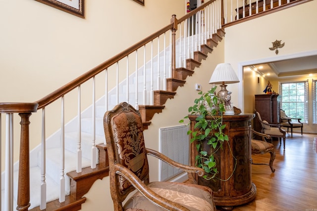 stairway with visible vents, crown molding, a high ceiling, and wood finished floors