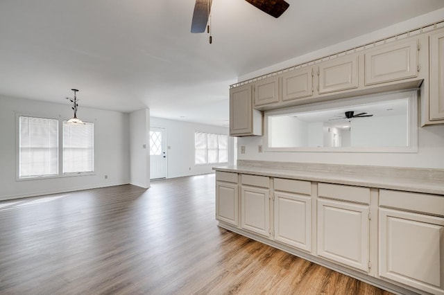 kitchen with baseboards, a ceiling fan, open floor plan, light countertops, and light wood-type flooring