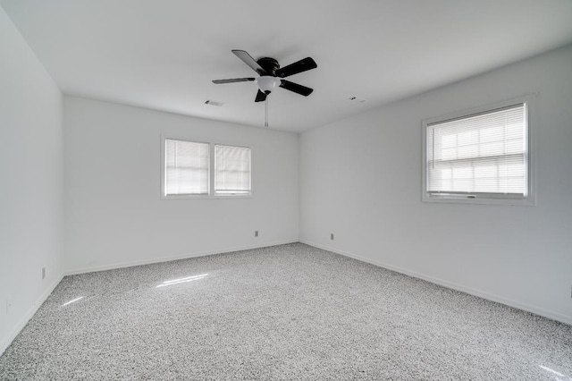 empty room featuring a ceiling fan, a wealth of natural light, visible vents, and baseboards