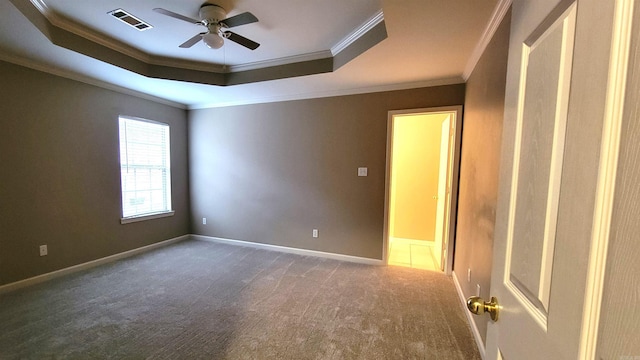 empty room with a tray ceiling, visible vents, a ceiling fan, carpet flooring, and baseboards