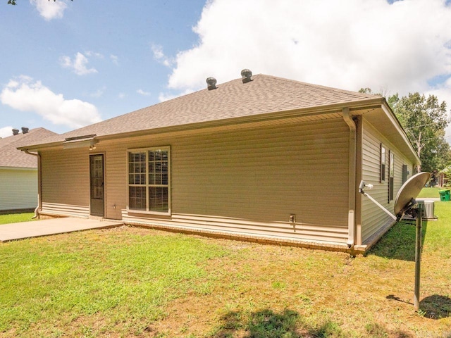 rear view of house featuring a shingled roof, a lawn, and a patio