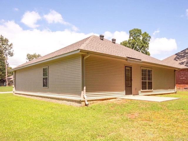 rear view of house with a shingled roof, a lawn, and a patio