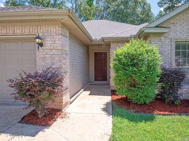 doorway to property featuring an attached garage, a shingled roof, and brick siding