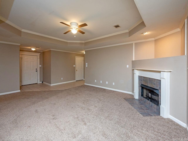 unfurnished living room with ceiling fan, light colored carpet, a tray ceiling, a tiled fireplace, and crown molding