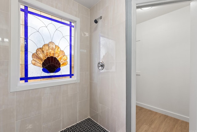 full bath with a tile shower, baseboards, and wood finished floors