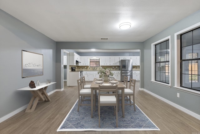 dining space with wood finished floors, visible vents, and baseboards