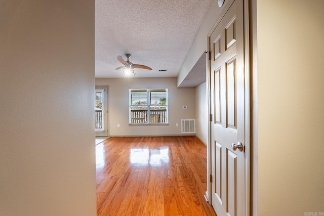 empty room featuring light wood finished floors, visible vents, baseboards, ceiling fan, and a textured ceiling