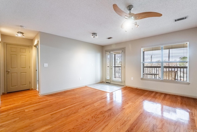 empty room featuring a textured ceiling, a ceiling fan, baseboards, visible vents, and light wood-style floors