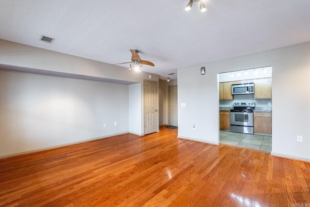 unfurnished living room featuring baseboards, visible vents, ceiling fan, a textured ceiling, and light wood-type flooring