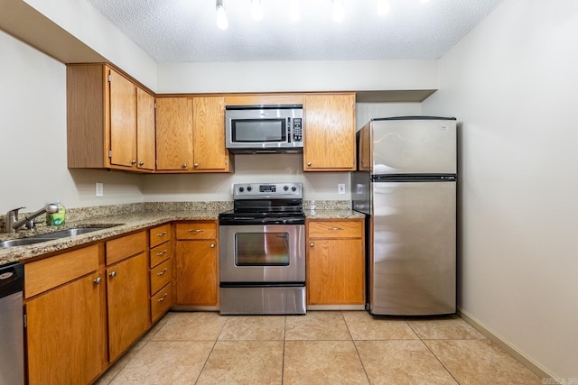 kitchen featuring appliances with stainless steel finishes, brown cabinetry, a sink, and a textured ceiling