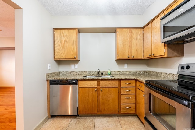 kitchen with a textured ceiling, appliances with stainless steel finishes, a sink, and light stone counters