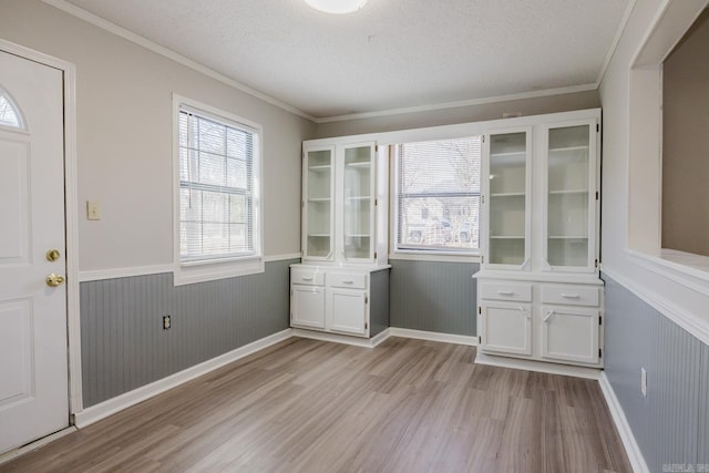 unfurnished dining area with ornamental molding, a wainscoted wall, light wood finished floors, and a textured ceiling