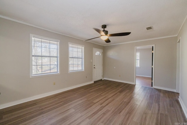 spare room featuring crown molding, wood finished floors, visible vents, and baseboards