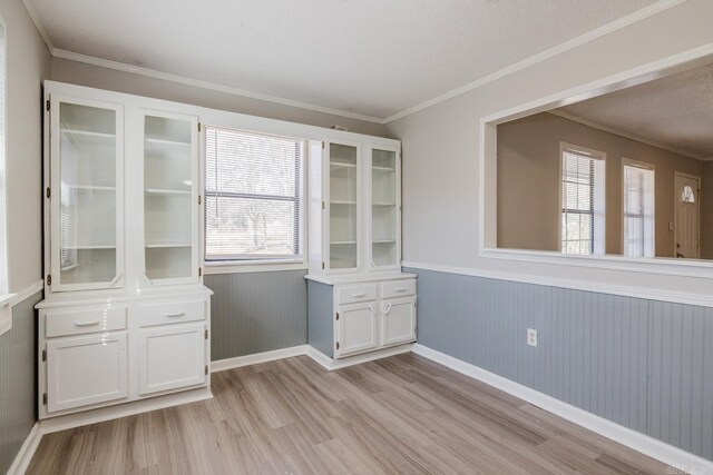 unfurnished dining area featuring light wood-type flooring, baseboards, wainscoting, and crown molding