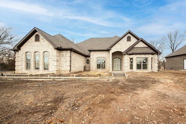 french country home featuring brick siding and roof with shingles