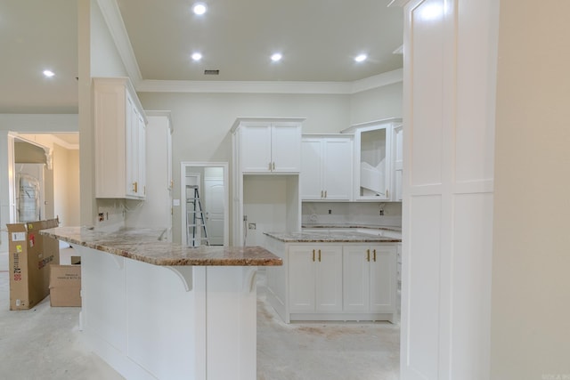 kitchen with light stone counters, a peninsula, white cabinetry, unfinished concrete flooring, and a kitchen bar