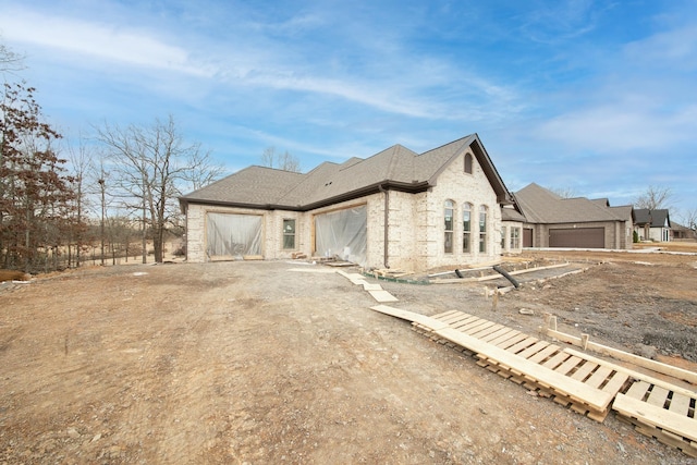 view of home's exterior with an attached garage, a shingled roof, dirt driveway, and brick siding