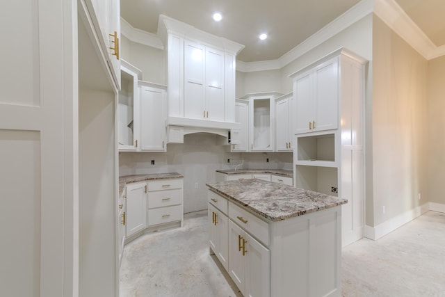 kitchen with light stone counters, white cabinets, crown molding, and baseboards