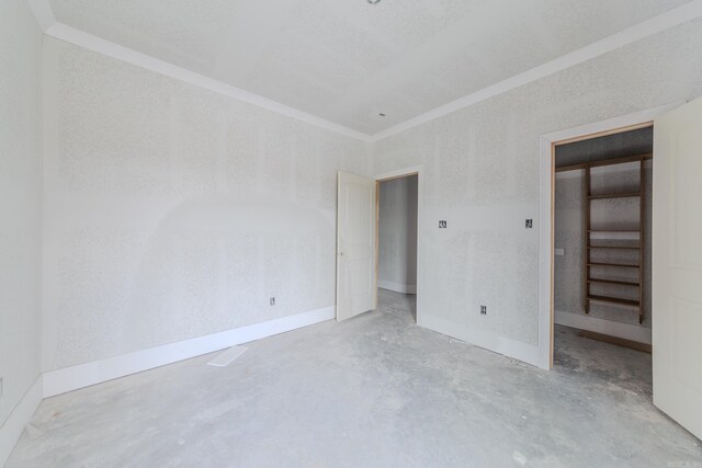 unfurnished bedroom with concrete flooring, a walk in closet, ornamental molding, and baseboards