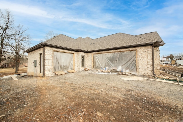 exterior space featuring driveway, a shingled roof, a garage, and brick siding