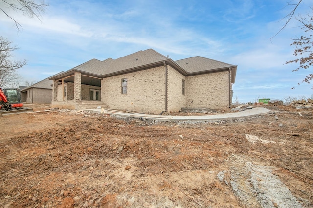 back of house with brick siding and roof with shingles