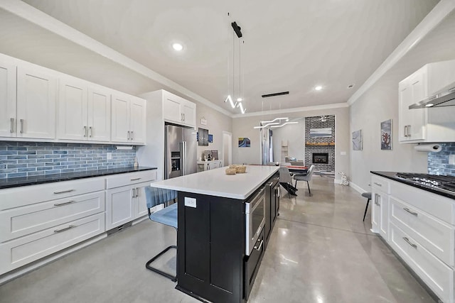 kitchen featuring a fireplace, white cabinetry, appliances with stainless steel finishes, tasteful backsplash, and finished concrete floors