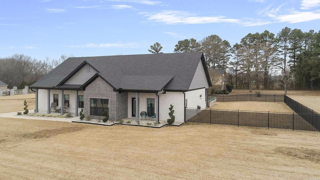 view of front of house featuring brick siding, a front lawn, a shingled roof, and fence private yard