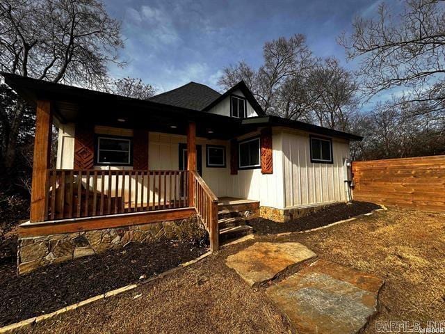 view of front facade with covered porch, roof with shingles, and fence