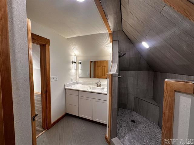 bathroom featuring baseboards, tiled shower, lofted ceiling, and vanity