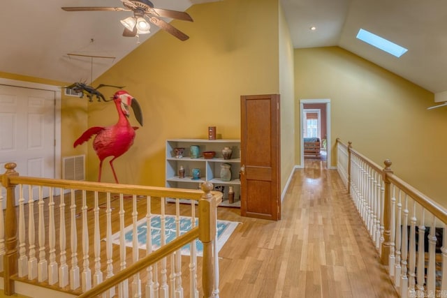 hallway featuring high vaulted ceiling, a skylight, light wood-style flooring, and an upstairs landing