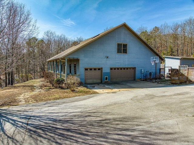 view of home's exterior with covered porch, driveway, an attached garage, and a wall unit AC
