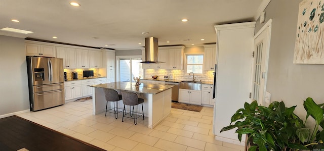 kitchen with stone countertops, a kitchen island with sink, island range hood, a kitchen breakfast bar, and appliances with stainless steel finishes