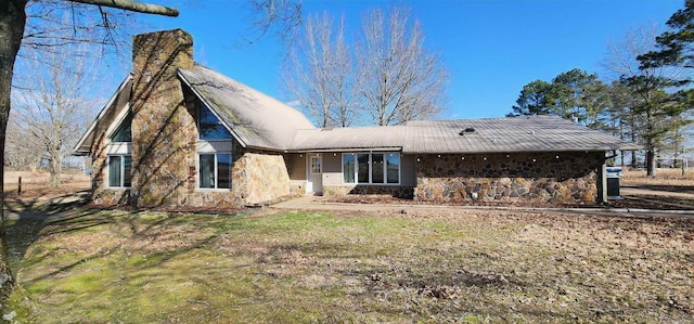 back of house featuring metal roof, stone siding, and a chimney