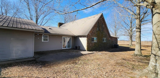 back of property featuring central AC, metal roof, a chimney, and a patio