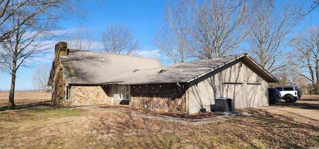 view of side of property featuring a garage, stone siding, central AC, and a chimney