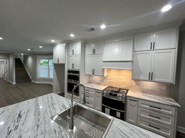 kitchen with premium range hood, a sink, visible vents, appliances with stainless steel finishes, and light stone countertops