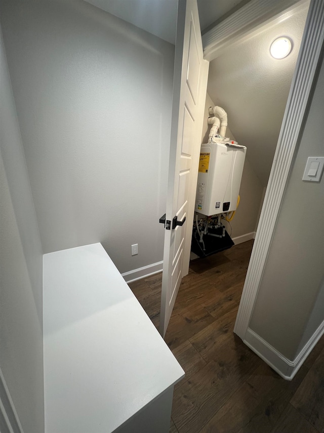 hallway featuring dark wood-type flooring, tankless water heater, vaulted ceiling, and baseboards