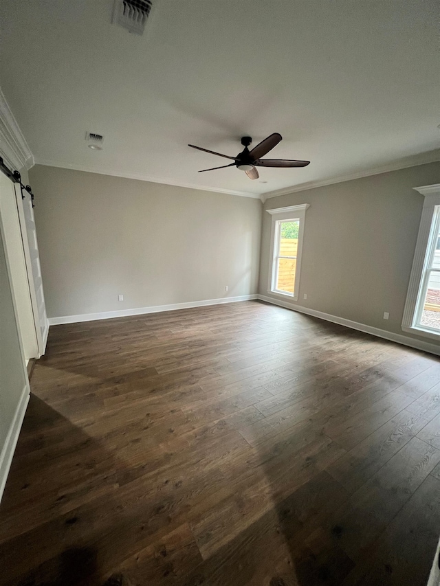 unfurnished room featuring dark wood finished floors, visible vents, a barn door, ornamental molding, and ceiling fan